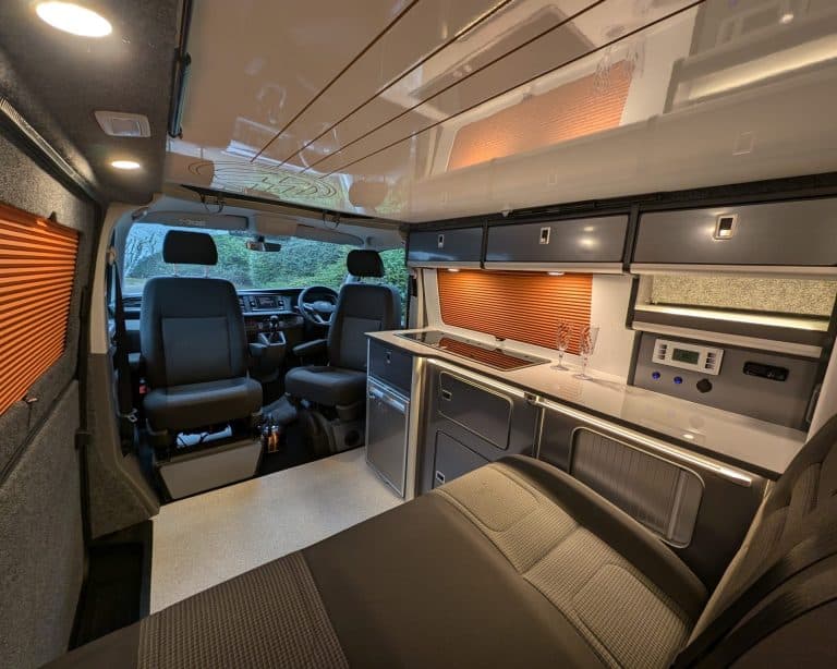 Interior of a campervan with kitchen, seating, and storage for travel and camping.