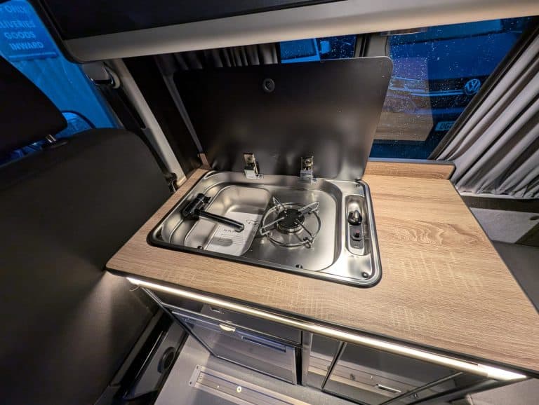 Portable camping stove and countertop setup in camper van.