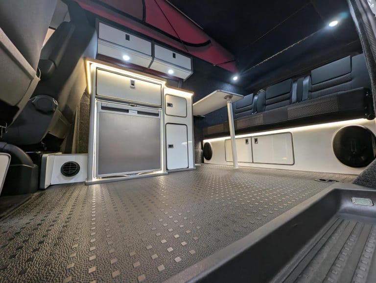 Interior of a custom van conversion featuring a compact kitchen, seating area, and modern amenities.